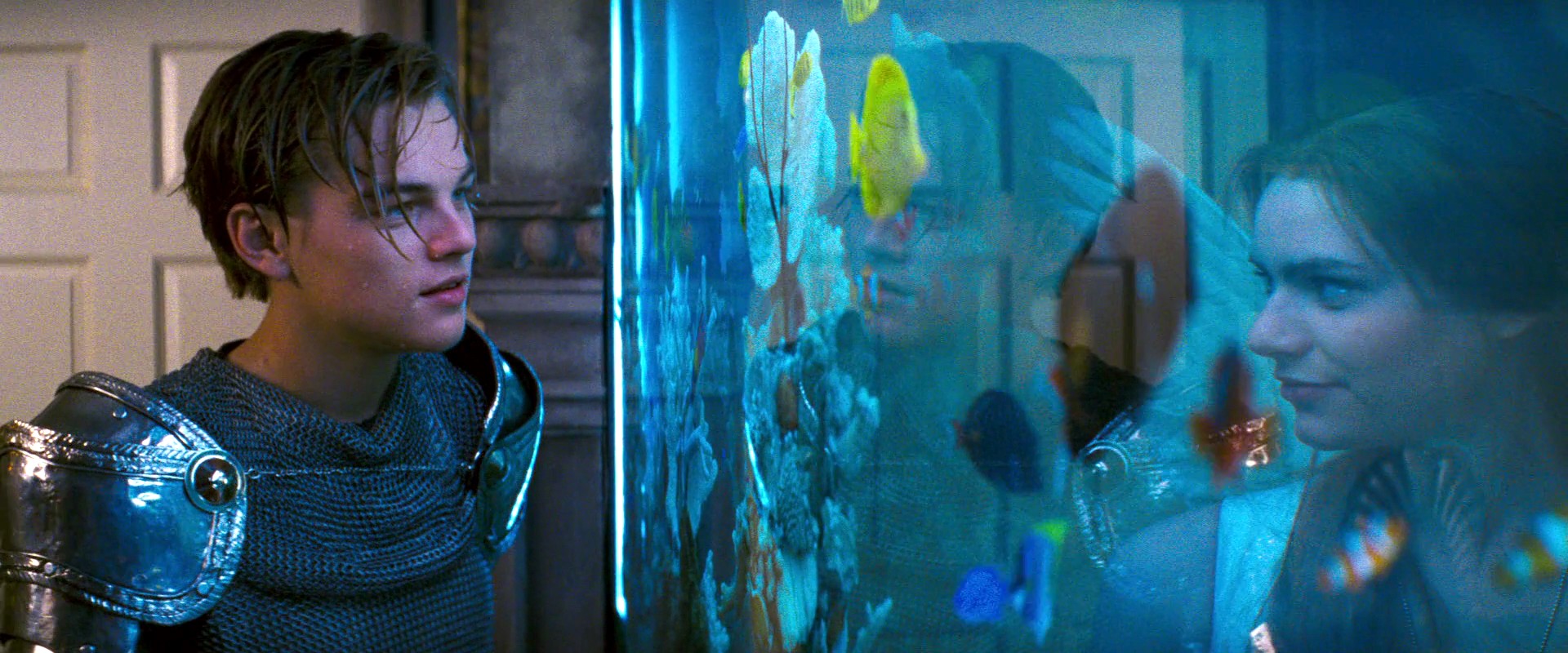 Romeo, in a costume of knight in shining knight armor, and Juliet, dressed as an angel with white wings, meet each other for the first time as a masked ball. They discover each other’s presence through an aquarium. Romeo stands to the left of the frame. The right of the frame is taken up entire by the fish tank, with tropical fish swimming near Juliet’s face.