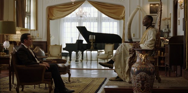 In this early scene in Green Book, the Black pianist Dr. Don Shirley is clad in an opulent, gold and white robe and sits on a chair with a tall back that looks like a throne. He meets a white working-class man named Tony Lip who is being interviewed for the job of Dr. Shirley’s chauffeur. In the background is a grand piano and the room is decked out with exotic art collections.